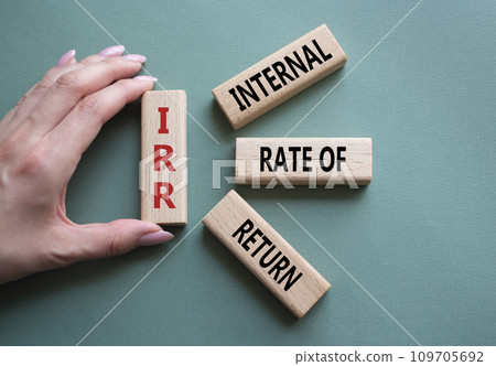 IRR - Internal Rate of Return symbol. Concept word IRR on wooden cubes. Businessman hand. Beautiful grey green background. Business and IRR concept. Copy space. 109705692