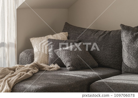 White and grey textured decorative pillows, cozy knitted blanket on a .dark grey sofa. Wabi-sabi interior details for decoration White and grey textured decorative pillows, cozy knitted blanket on a .dark grey sofa. Wabi-sabi interior details for decoration 109706078