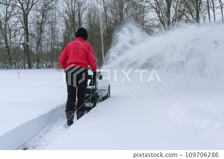 A young woman clears snow with snow removal equipment after a heavy snowfall A young woman clears snow with snow removal equipment after a heavy snowfall 109706286