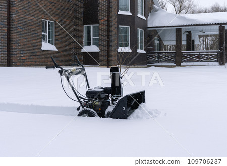 A gasoline snowplow on the background of a house after a heavy snowfall A gasoline snowplow on the background of a house after a heavy snowfall 109706287