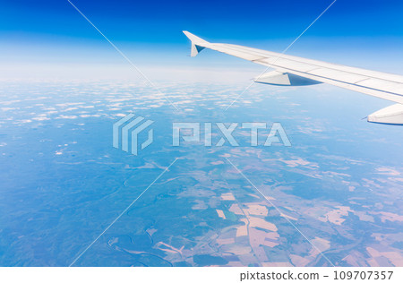 Aerial view from airplane window above green ground. View from the airplane window with beautiful clouds at sunrise Aerial view from airplane window above green ground. View from the airplane window with beautiful clouds at sunrise 109707357