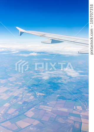 Aerial view from airplane window above green ground. View from the airplane window with beautiful clouds at sunrise Aerial view from airplane window above green ground. View from the airplane window with beautiful clouds at sunrise 109707358
