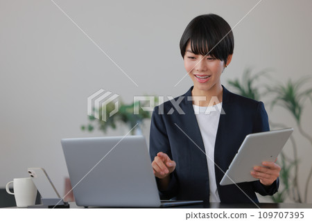 拿著平板電腦並指著 PC 1 的女商人 109707395