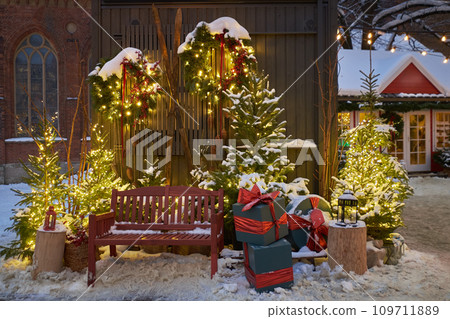 Christmas decorations - bench, Christmas trees, gift boxes, garlands and lights. Festive Christmas decoration at the Dome Square in old Riga city. Riga, Latvia. Snowy New Year's photo location. Christmas decorations - bench, Christmas trees, gift boxes, garlands and lights. Festive Christmas decoration at the Dome Square in old Riga city. Riga, Latvia. Snowy New Year's photo location. 109711889