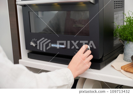 Female cooking hand operating a microwave oven Female cooking hand operating a microwave oven 109713432