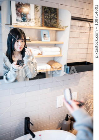 A woman applying makeup through the mirror in the bathroom 109714003