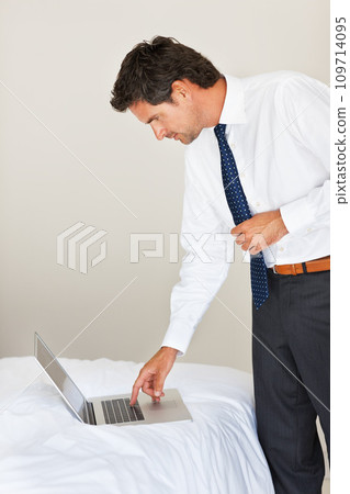 Laptop, bedroom and a business man getting ready for work at his home in the morning while checking an email. Corporate, computer on a bed and a professional employee dressing in his apartment Laptop, bedroom and a business man getting ready for work at his home in the morning while checking an email. Corporate, computer on a bed and a professional employee dressing in his apartment 109714095