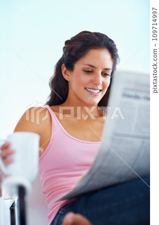 Happy woman, reading and newspaper with coffee and morning headlines for wellness in living room. Young person, smile and espresso to relax on weekend and current events with warm drink in apartment Happy woman, reading and newspaper with coffee and morning headlines for wellness in living room. Young person, smile and espresso to relax on weekend and current events with warm drink in apartment 109714997