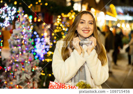 Happy woman choosing Christmas decoration at Christmas street market in evening Happy woman choosing Christmas decoration at Christmas street market in evening 109715456