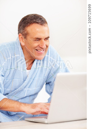 Bathrobe, morning and mature happy man on laptop for email, social media or streaming subscription on sofa. Internet search, couch and senior person on computer, website or networking in living room. Bathrobe, morning and mature happy man on laptop for email, social media or streaming subscription on sofa. Internet search, couch and senior person on computer, website or networking in living room. 109715699