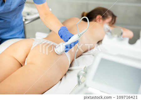 Anti-cellulite therapy massage and shrink pores and repair damaged skin device in spa salon. Professional cosmetologist works with woman figure correction Anti-cellulite therapy massage and shrink pores and repair damaged skin device in spa salon. Professional cosmetologist works with woman figure correction 109716421