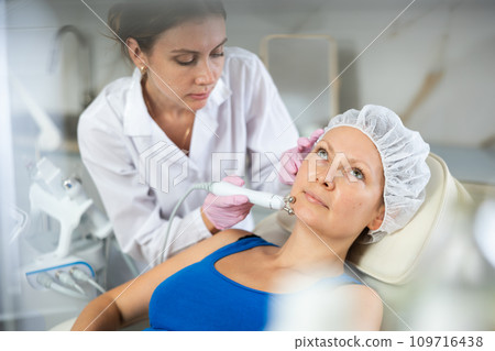Young female cosmetologist doing microcurrent procedure to adult woman Young female cosmetologist doing microcurrent procedure to adult woman 109716438