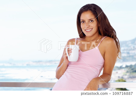 Portrait, smile and woman drinking coffee at balcony in home, mockup or space. Face, tea cup and happy person at terrace with healthy beverage, espresso or latte by ocean to relax in the morning 109716887