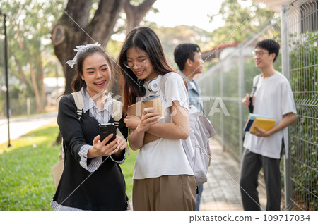 Two young Asian female students are enjoying talking while walking on a footpath on their campus. 109717034