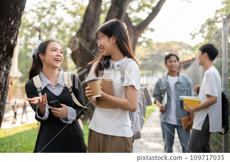 Two young Asian female students are enjoying talking while walking on a footpath on their campus. 109717035