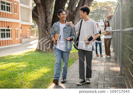 Two cheerful Asian male students are enjoying talking while walking to school together. Two cheerful Asian male students are enjoying talking while walking to school together. 109717045