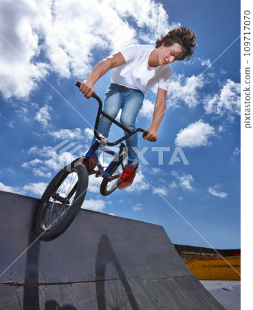 Bike, jump and teen on ramp for sport performance, ride or training for event at park with sky. Bicycle, stunt or kid balance on edge of board for cycling trick in competition or challenge with risk Bike, jump and teen on ramp for sport performance, ride or training for event at park with sky. Bicycle, stunt or kid balance on edge of board for cycling trick in competition or challenge with risk 109717070