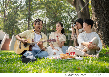 Group of cheerful diverse young Asian friends are enjoying picnicking in a beautiful park together. Group of cheerful diverse young Asian friends are enjoying picnicking in a beautiful park together. 109717112