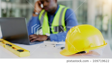 Engineering, construction tools and architect with helmet on desk with break from project, worksite or renovation. African, person or foreman with laptop to review of plans, building or real estate Engineering, construction tools and architect with helmet on desk with break from project, worksite or renovation. African, person or foreman with laptop to review of plans, building or real estate 109719622