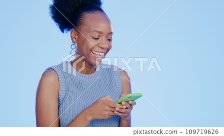 Phone, smile and black woman in a studio networking on social media, mobile app or the internet. Technology, happy and young African female model scroll on website with cellphone by blue background. 109719626