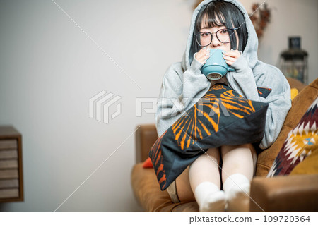 Woman sitting on sofa drinking hot drink 109720364