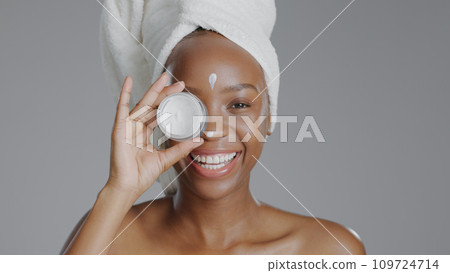 Woman, moisturizer and smile in portrait for skincare or beauty, health and wellness or dermatology. Happy black person, skin and cosmetics with glow, care and lotion in studio by gray background Woman, moisturizer and smile in portrait for skincare or beauty, health and wellness or dermatology. Happy black person, skin and cosmetics with glow, care and lotion in studio by gray background 109724714
