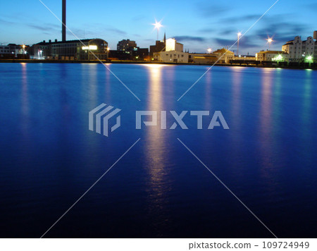 Ocean, night and buildings in port with lights, reflection on calm blue water or holiday location. City at sea in evening, travel, skyline and nature, urban beach village for vacation, peace and view Ocean, night and buildings in port with lights, reflection on calm blue water or holiday location. City at sea in evening, travel, skyline and nature, urban beach village for vacation, peace and view 109724949