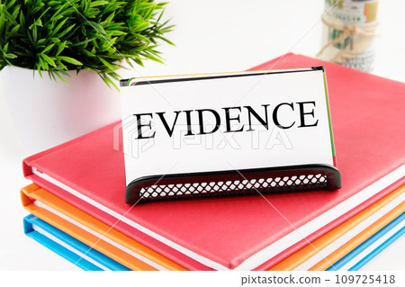 EVIDENCE text on a white business card standing on a stand on notebooks, next to the money out of focus and a green plant on a white background 109725418