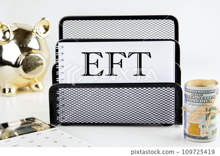 EFT text on a white piece of paper next to a piggy bank, a roll of money and a calculator on a white background EFT text on a white piece of paper next to a piggy bank, a roll of money and a calculator on a white background 109725419