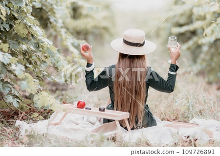 Woman picnic vineyard. Happy woman with a glass of wine at a picnic in the vineyard, wine tasting at sunset and open nature in the summer. Romantic dinner, fruit and wine. 109726891