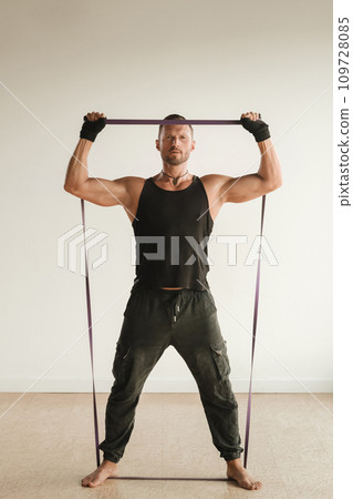 A man in black sportswear is engaged in strength fitness using a rubber loop indoors 109728085
