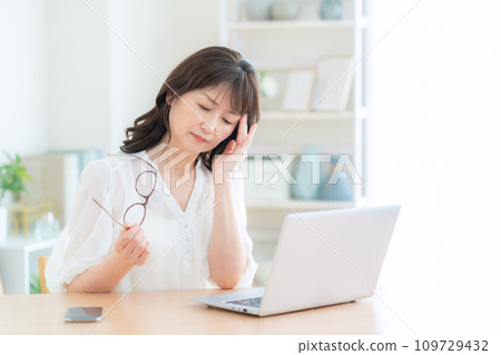 A middle-aged woman with tired eyes using a computer in the living room A middle-aged woman with tired eyes using a computer in the living room 109729432