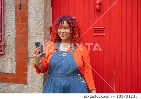 Young Femele holding smartphone against red door Young Femele holding smartphone against red door 109731235