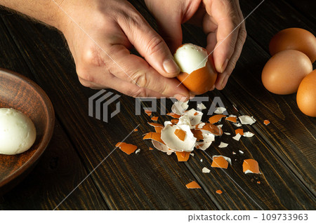 Cooking a delicious lunch with boiled eggs on the kitchen table. Shelling an egg with the hands of a chef 109733963