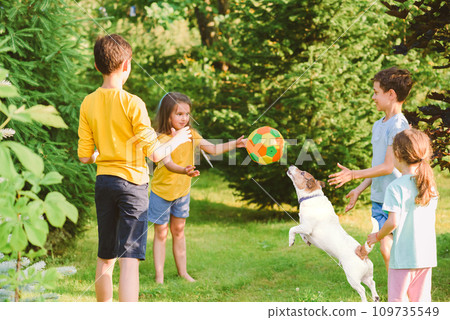 Group of children throw and catch a ball while playing "Monkey in the Middle" game with a dog 109735549