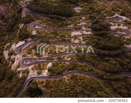Aerial drone top down view of serpentine road in Kotor bay, Montenegro. Vehicles drive on winding mountain road leading to the Lovchen mountain. Low car traffic. Summer green forest around. Aerial drone top down view of serpentine road in Kotor bay, Montenegro. Vehicles drive on winding mountain road leading to the Lovchen mountain. Low car traffic. Summer green forest around. 109736401