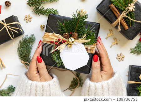 Hands with Christmas present with blank gift tag, with fir branches and decor, Mockup Hands with Christmas present with blank gift tag, with fir branches and decor, Mockup 109736753