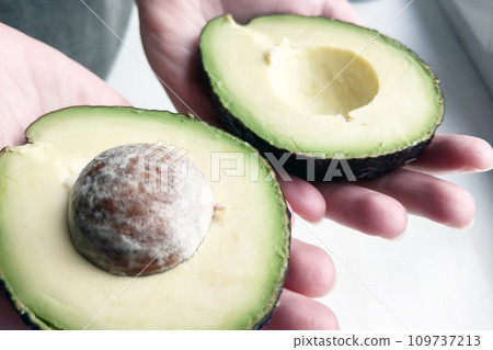 A girl holds two halves of an avocado in her hands. 109737213