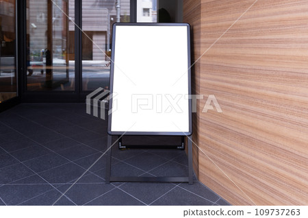 Blank white outdoor advertising stand/sandwich board mock up template. Clear street signage board placed by an outdoor dinning area of a restaurant. Background texture of standee on street. Blank white outdoor advertising stand/sandwich board mock up template. Clear street signage board placed by an outdoor dinning area of a restaurant. Background texture of standee on street. 109737263