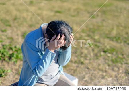 Senior woman holding her head, park, exercise, future, anxiety, worries 109737968
