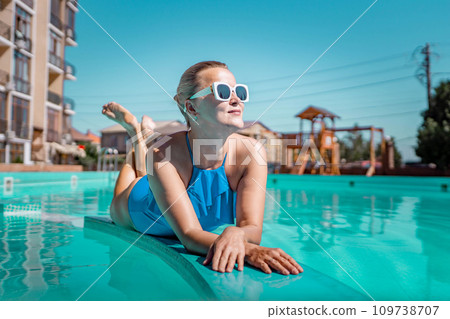 Bikini-clad woman enjoys poolside relaxation. Poolside ambiance. Capturing woman's relaxed time near pool. Bikini-clad woman enjoys poolside relaxation. Poolside ambiance. Capturing woman's relaxed time near pool. 109738707
