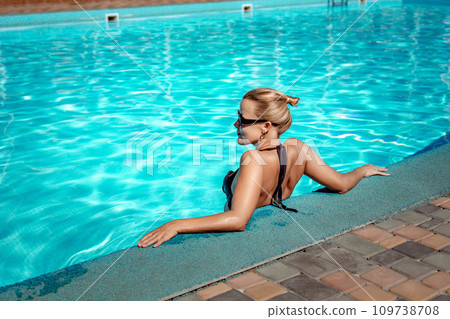 Bikini-clad woman enjoys poolside relaxation. Poolside ambiance. Capturing woman's relaxed time near pool. Bikini-clad woman enjoys poolside relaxation. Poolside ambiance. Capturing woman's relaxed time near pool. 109738708