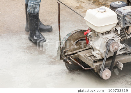Worker using diamond saw blade machine cutting concrete road at construction site 109738819