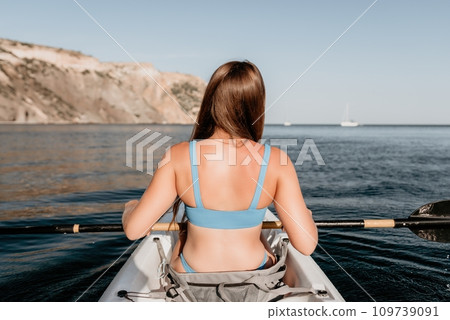 Woman in kayak back view. Happy young woman with long hair floating in kayak on calm sea. Summer holiday vacation and cheerful female people relaxing having fun on the boat. 109739091