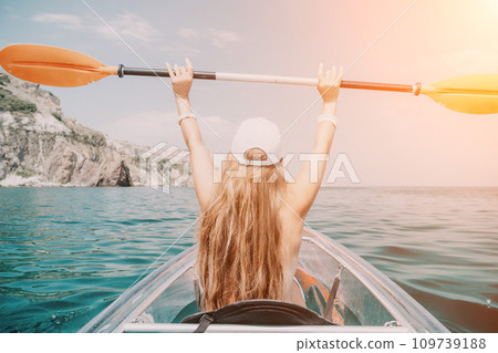 Woman in kayak back view. Happy young woman with long hair floating in transparent kayak on the crystal clear sea. Summer holiday vacation and cheerful female people relaxing having fun on the boat 109739188