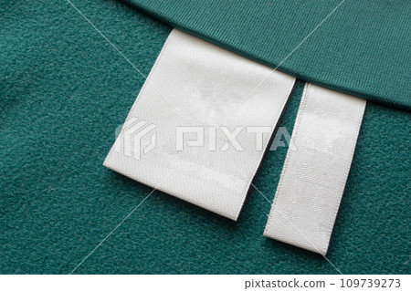 Blank white laundry care clothes label on green fabric texture background 109739273