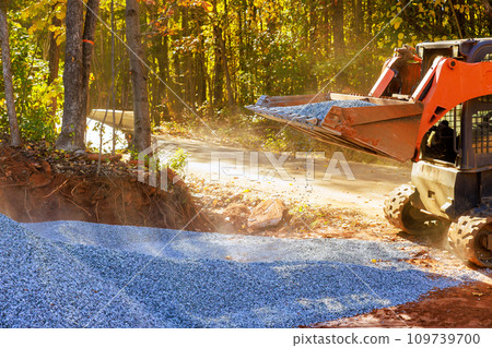 Preparation of base for new road consists laying crushed stone gravel filled up with by tractor Preparation of base for new road consists laying crushed stone gravel filled up with by tractor 109739700