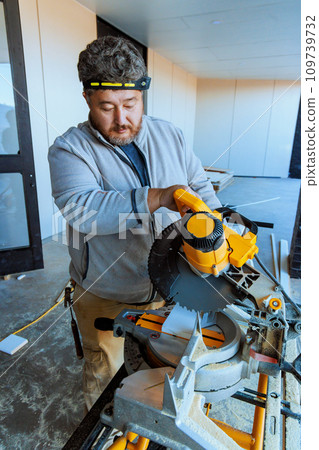Trim worker using chop saw to cuts wooden base moldings 109739732