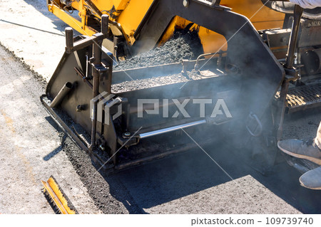 Pavement machine lays fresh bitumen asphalt on top of gravel base during highway construction 109739740