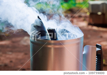 Using barbecue chimney starter to get charcoal ready for cooking on grill, which is glowing hot 109739800